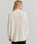 A woman with blonde hair wears the Oversized Cotton Fisherman sweater, shown from behind against a plain light background.