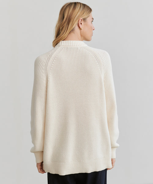 A woman with blonde hair wears the Oversized Cotton Fisherman sweater, shown from behind against a plain light background.