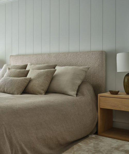 A cozy bedroom featuring the Pacific Bed with a Belgian linen bedspread, neutral pillows, a wooden nightstand with a white lamp and brown bowl, set against a light gray paneled wall.