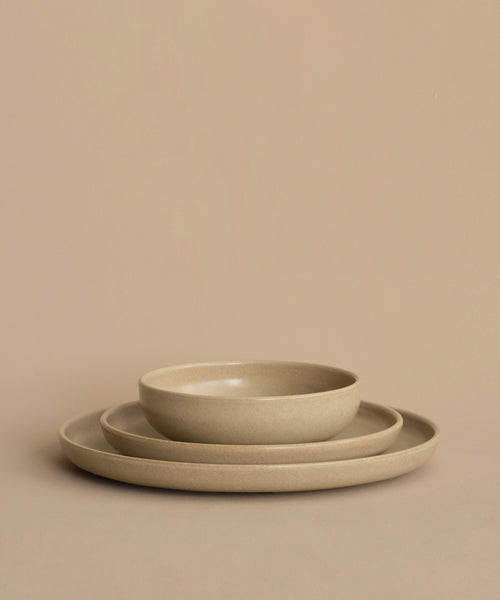Three beige ceramic dishes are stacked against a matching background. The set includes a large plate, a smaller plate, and the Pacific Breakfast Bowl—a versatile and stylish stoneware bowl—arranged perfectly on top.