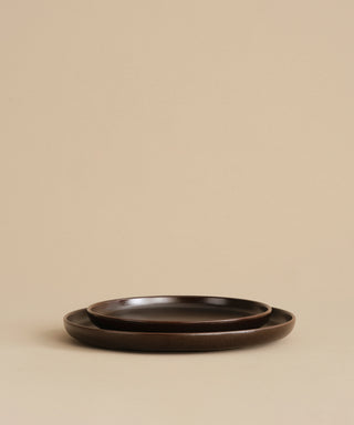 Two nested Pacific Salad Plates in dark brown from the Pacific collection rest on a beige surface against a plain beige background.