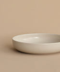 The Pacific Soup Bowl, a simple round and shallow white stoneware piece, rests on a beige surface with a matching beige background.