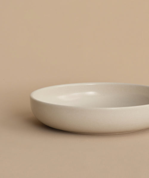 The Pacific Soup Bowl, a simple round and shallow white stoneware piece, rests on a beige surface with a matching beige background.