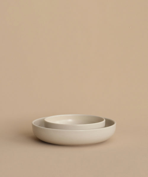 Two round, light beige Pacific Soup Bowls of different sizes are nested together on a matching beige surface with a plain beige background. Made of stoneware in Portugal.