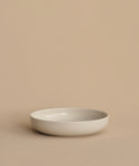 A simple, round, shallow white Pacific Soup Bowl is displayed on a beige surface against a matching background, highlighting its minimalistic, pattern-free elegance.