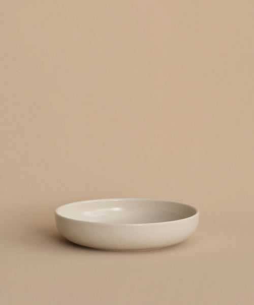 A simple, round, shallow white Pacific Soup Bowl is displayed on a beige surface against a matching background, highlighting its minimalistic, pattern-free elegance.