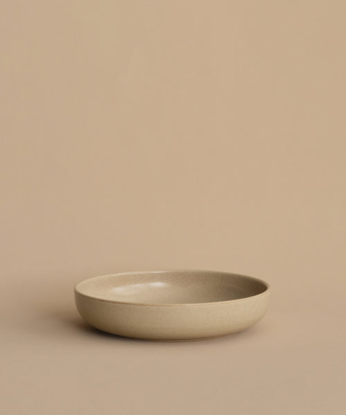 The Pacific Soup Bowl is a plain, shallow beige stoneware piece displayed on a matching beige surface with a neutral beige background.