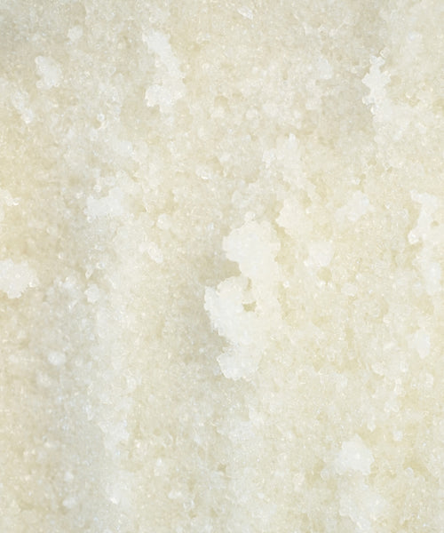 Close-up of coarse, white granules in Perfecting Body Scrub, featuring an uneven crystalline texture—ideal for exfoliating and hydrating skincare rituals.