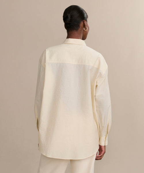 A person faces away, wearing the cream-colored Pierce Shirt—made from textured cotton in a loose fit with a collar and matching pants—against a plain beige background.