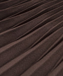Close-up of the Pleated Skirt in brown, showing detailed texture and diagonal pleats that create raised and recessed lines across the fabric.