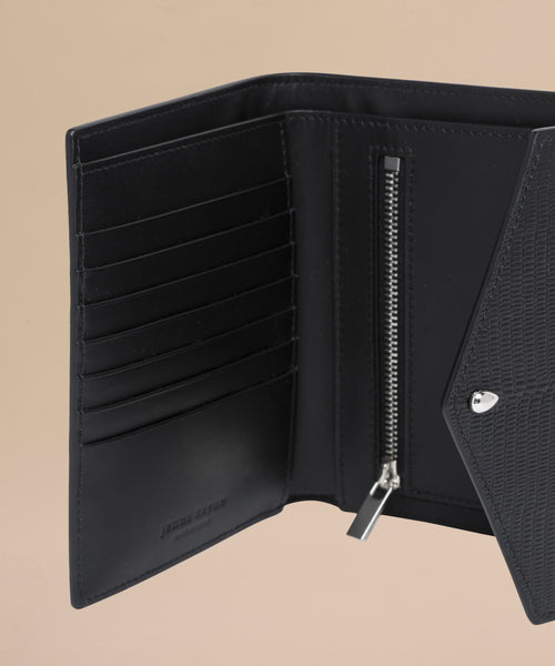 A close-up of the Reece Leather Wallet, a mid-size black wallet with card slots, zippered compartment, and textured flap, displayed open against a beige background.