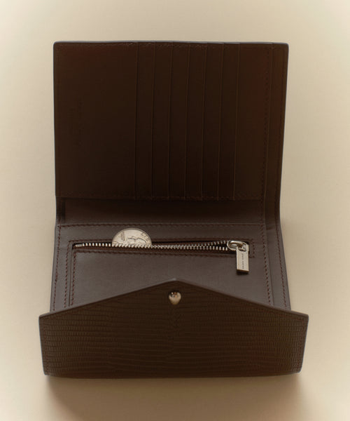 The Reece Leather Wallet in brown embossed leather is open, displaying card slots, a zippered coin pocket with coins, and a snap button closure.