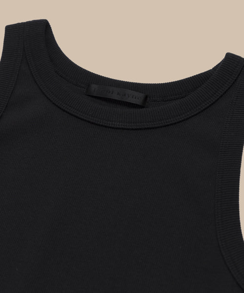 Close-up of the Cotton Rib Tank in black, featuring a round neckline and heavy rib texture. Laid flat on a beige background, this soft cotton blend layering top has a black tag at the neckline.