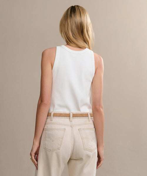 A woman with blonde hair, seen from behind, wears a Cotton Rib Tank in white and light beige high-waisted jeans against a plain neutral background.