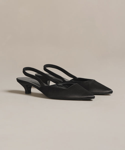 The Satin Kitten Heel, an elegant pair of black satin slingbacks with pointed toes and kitten heels made in Italy, is showcased on a light neutral background.