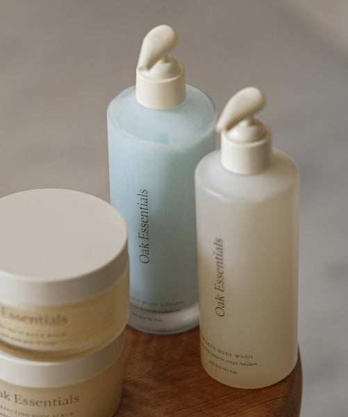 Two pump bottles and two jars of Oak Essentials Silk Body Duo are arranged on a wooden surface. The minimalist white packaging highlights their skin-soothing formulas for ultimate hydration.