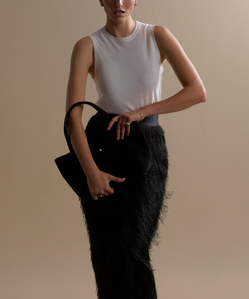 A woman in a sleeveless white top and the Sterling Skirt holds a black handbag in front of her against a plain beige background, with her face partially out of frame.