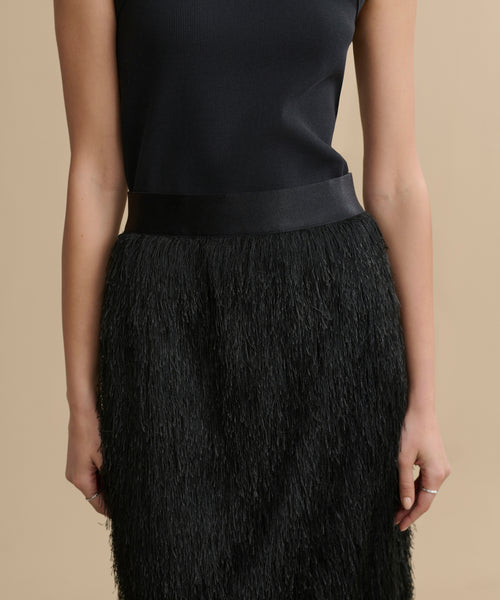 A person wears a sleeveless black top with the Sterling Skirt, a textured, fringed black pencil-style skirt, against a beige background. Only the torso and upper legs are shown.