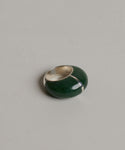 The Division Ring is a chunky designer ring with a sterling silver band and a bold, glossy green enamel section, showcasing sculptural silhouettes and displayed on a light grey textured surface.