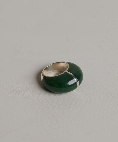 The Division Ring is a chunky designer ring with a sterling silver band and a bold, glossy green enamel section, showcasing sculptural silhouettes and displayed on a light grey textured surface.