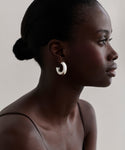 A woman with dark skin and slicked-back hair in a low bun models the Large Donut Hoops, shown in profile against a light neutral background and wearing a thin-strapped top.