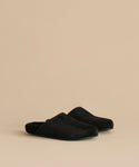 The Suede Ashby Clog—black slip-on clogs with closed toes, open backs, and a cozy shearling-lined footbed—is displayed on a plain beige background.
