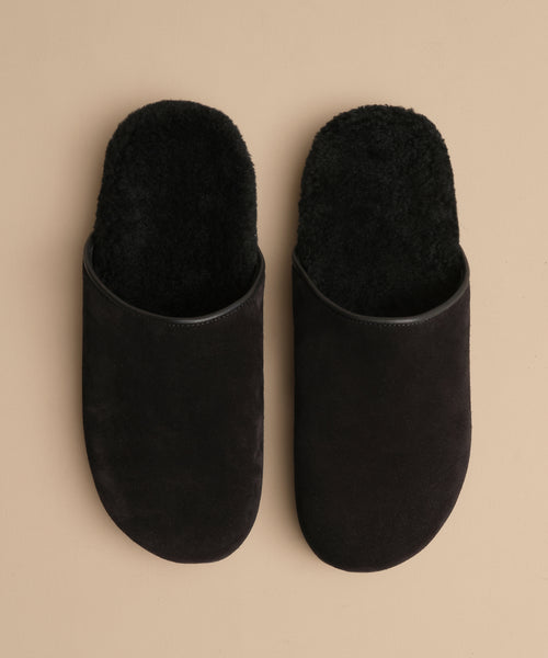 A pair of Suede Ashby Clogs in black with a fuzzy texture and a cozy shearling-lined footbed, displayed side by side on a beige background.