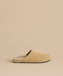 The Suede Ashby Clog features tan suede, a fluffy shearling-lined footbed, and a black sole, shown on a matching beige background.