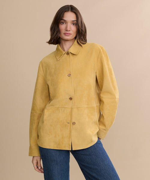 A person with shoulder-length brown hair wears the Suede Lennox Jacket in a honey shade and blue jeans, standing against a plain beige background.