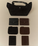 A black tote bag is showcased above six leather goods: two envelope wallets, two Suede Pouches in black and brown, and two slim rectangular card holders—all designed for stylish organization.
