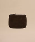 The Suede Pouch is a small, square, dark brown suede pouch with a silver zipper, shown against a plain beige background.