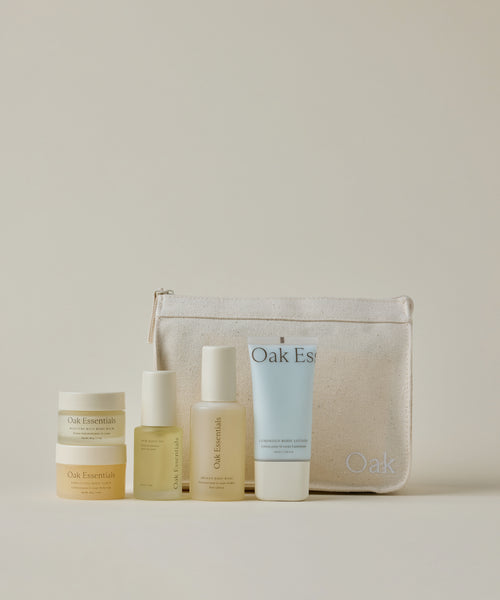 The Travel Body Routine includes a jar, two pump bottles, and a tube, all arranged before a beige fabric zip pouch with Oak embroidery. TSA-approved and perfect for convenient on-the-go skincare.