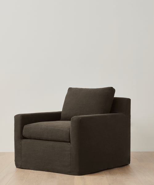 A Harbor Chair with dark brown cushioned linen upholstery and a boxy silhouette is placed on a light wood floor against a simple off-white wall.