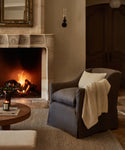 A cozy fireplace scene featuring the Miramar Chair, skillfully handmade in the USA with Belgian linen for timeless comfort and elegance.