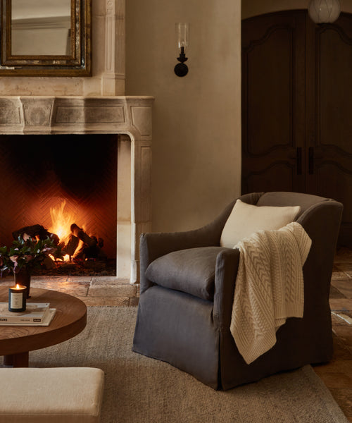 A cozy fireplace scene featuring the Miramar Chair, skillfully handmade in the USA with Belgian linen for timeless comfort and elegance.