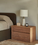 The Palms Nightstand, crafted in walnut and adorned with a lamp and candles, brings warmth and elegance to any space.