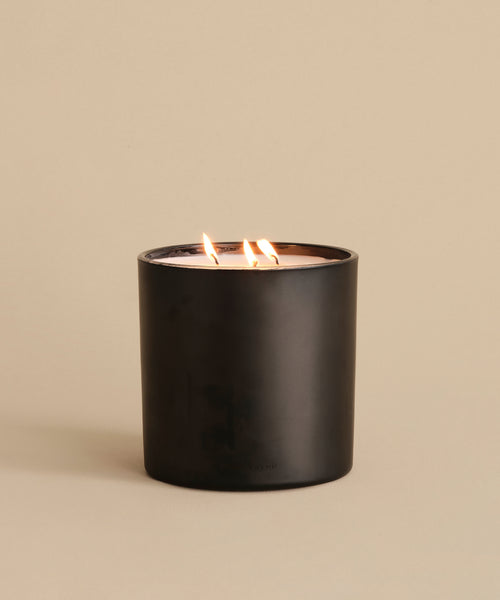An Extra Large Topanga Glass Candle in black matte sits on a beige surface with three wicks lit, highlighting this hand-poured Los Angeles creation against a matching background.