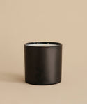 The Extra Large Topanga Glass Candle features a sleek black cylindrical design with three wicks. Hand-poured in Los Angeles, it is displayed on a beige surface with a matching beige background.