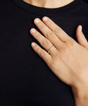 A person wearing a dark shirt rests their left hand on their chest, showcasing the Stevie Grey Diamond Band with small stones on their ring finger—a perfect piece of fine jewelry.