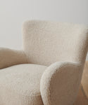 A close-up of the Aspen Chair, featuring plush cream-colored textured boucle fabric in a mid-century modern design, placed on a wooden floor with a plain white wall backdrop.