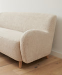 The Aspen Sofa with rounded armrests and wooden legs sits on a light wood floor against a plain white wall.
