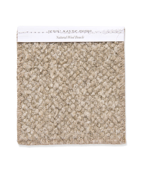 A square swatch of textured, looped beige wool with frayed edges, labeled “Fabric Swatch Natural Wool Boucle” on a white strip—ideal for Jenni Kayne Furniture or an upholstered bench.