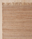 A close-up view of the rectangular Arrowhead Jute Rug, featuring fringe on one end, displayed on a light wooden floor.