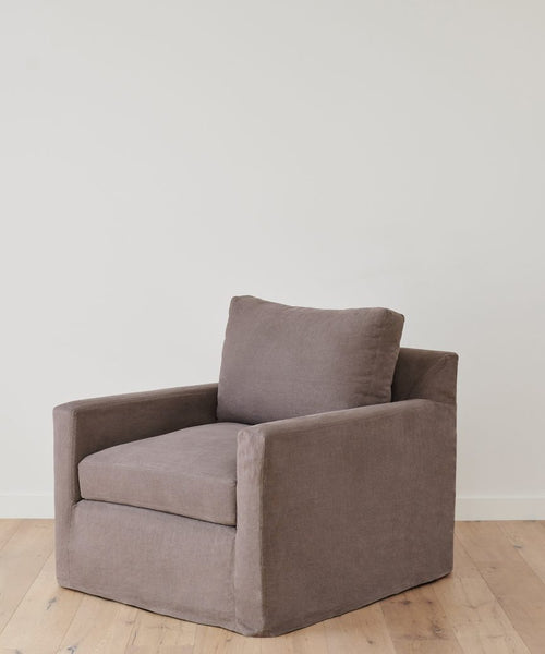 The Harbor Chair, handmade in Los Angeles, features a modern charcoal linen design with cushioned seat and backrest, shown on a light wooden floor against a white wall—blending comfort and contemporary style.