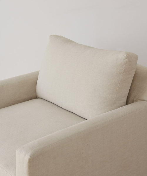 The Harbor Chair, handmade in Los Angeles, features beige upholstery, a plush back cushion, and minimalist lines, shown against a plain white background.