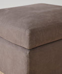 A close-up of the Harbor Ottoman in charcoal linen highlights its visible stitching and soft, cushioned top.