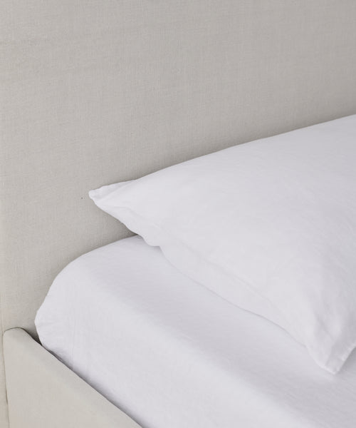 A close-up of the Pacific Bed, featuring a neatly made bed with a white pillow and sheet, set against a light beige upholstered headboard and complemented by a natural linen bed frame.