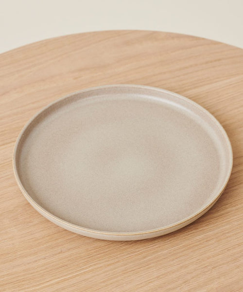 A plain, round, beige Pacific Platter stoneware serving plate rests on a light wooden surface, photographed from above.