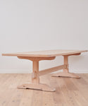 The Trestle Dining Table, crafted from Knotty Alder with a thick rectangular top and sturdy legs, stands on a light wooden floor against a plain white wall.