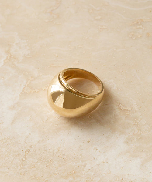 The Felix Dome Ring, crafted in 14k solid gold with a smooth, rounded surface, is displayed on a beige marble background.